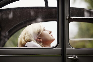 Woman looking up while sitting in vintage car - CAVF09540