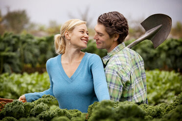 Romantischer Mann, der eine Schaufel hält und neben einer Frau auf einem Bauernhof steht - CAVF09550