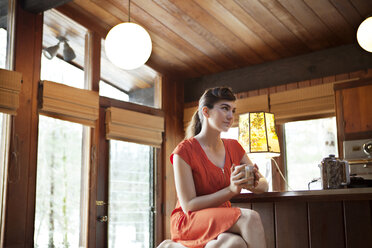 Frau hält Tasse, während sie am Tisch im Café sitzt - CAVF09603