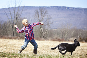 Junge spielt mit Hund auf einem Feld - CAVF09649