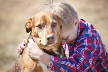Junge umarmt Hund auf dem Feld - CAVF09650