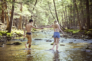 Young couple holding hands while walking in stream - CAVF09716