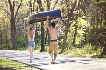 Rear view of couple carrying rowboat while walking on road in forest - CAVF09720