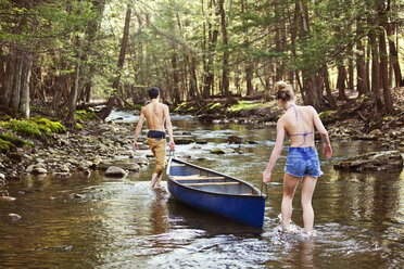 Couple carrying rowboat while walking in river - CAVF09727