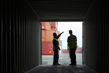 Arbeiter zeigt weg, während er mit einem Mann an einem Frachtcontainer an einem Handelsdock steht - CAVF09774