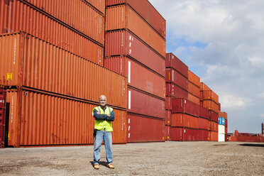 Portrait of confident man with arms crossed standing against cargo containers - CAVF09775