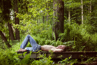 Mann ohne Hemd auf Pier im Wald liegend - CAVF09802