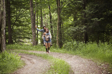 Frau nimmt Mann auf unbefestigtem Weg im Wald huckepack - CAVF09836