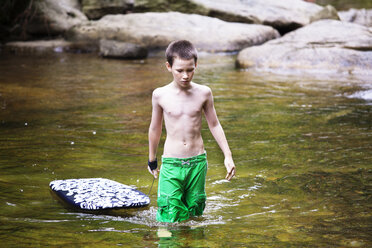 Junge ohne Hemd trägt Surfbrett beim Spaziergang im See - CAVF09858