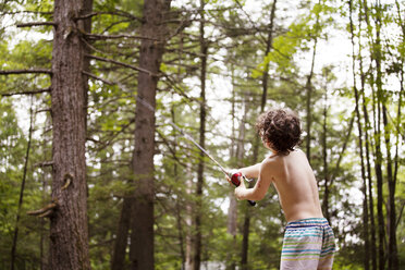 Rückansicht eines Jungen, der eine Angelrute auswirft, während er im Wald fischt - CAVF09864