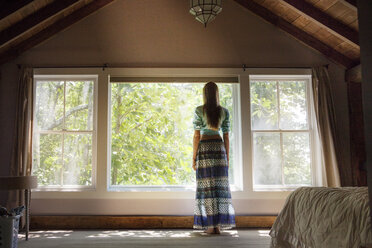 Rear view of woman standing by window at home stock photo