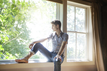 Thoughtful man sitting on window at home - CAVF09901