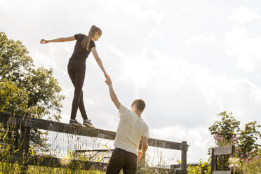 Man holding hand of woman walking on fence in farm - CAVF09923