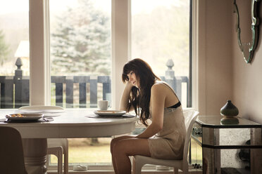 Side view of woman sitting on chair by table at home - CAVF09956