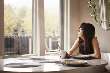 Frau schaut weg, während sie zu Hause am Frühstückstisch sitzt - CAVF09959