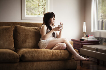 Frau mit Kaffeetasse entspannt auf Sofa - CAVF09960