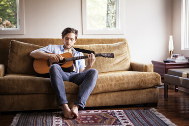 Mann spielt Gitarre, während er auf dem Sofa sitzt - CAVF09964