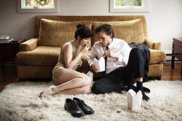 Paar isst Essen aus einem Karton, während es auf einem Teppich zu Hause sitzt - CAVF10003