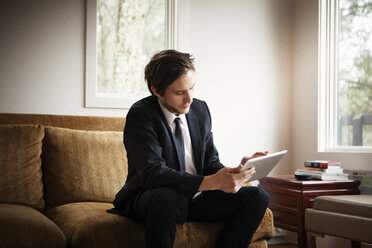 Geschäftsmann, der einen Tablet-Computer benutzt, während er zu Hause auf dem Sofa sitzt - CAVF10005