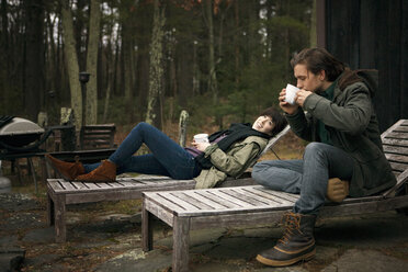 Frau sieht Mann an, der Kaffee trinkt, während er auf einem Liegestuhl sitzt - CAVF10016
