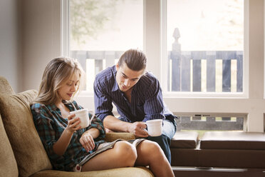Ehepaar liest eine Zeitschrift und trinkt zu Hause Kaffee - CAVF10028