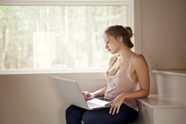 Frau, die einen Laptop benutzt, während sie zu Hause auf den Stufen sitzt - CAVF10047