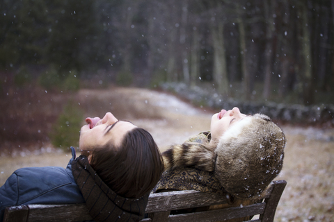 Verspieltes Paar streckt die Zunge heraus, während es auf einer Bank im Wald sitzt, lizenzfreies Stockfoto
