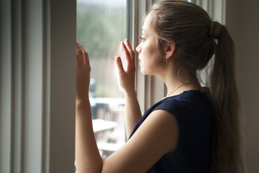 Frau schaut durch das Fenster zu Hause - CAVF10078