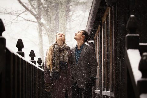 Pärchen, das im Winter am Zaun steht und nach oben schaut, lizenzfreies Stockfoto