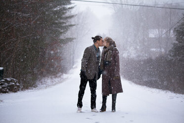 Romantisches Paar, das sich küsst, während es auf einem verschneiten Feld bei Schneefall steht - CAVF10084