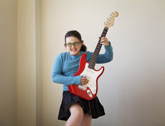 Fröhliches Mädchen spielt Gitarre an der Wand zu Hause - CAVF10104