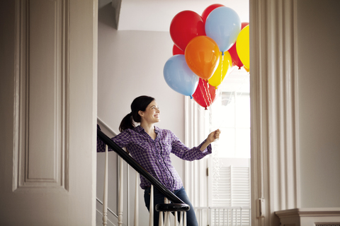 Happy woman standing by staircase while holding helium balloons stock photo