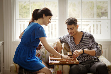 Paar spielt Backgammon, während es zu Hause auf einem Sessel sitzt - CAVF10149