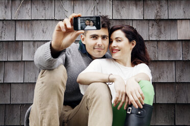 Mann und Frau nehmen Selfie beim Sitzen gegen hölzerne Wand - CAVF10162