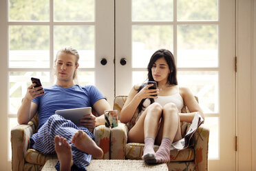 Ein Paar benutzt ein Mobiltelefon, während es zu Hause auf einem Sessel sitzt - CAVF10183