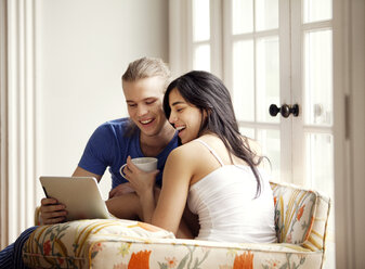 Cheerful couple looking at tablet computer while sitting on armchair - CAVF10184