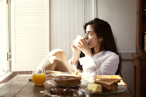 Nachdenkliche Frau trinkt Kaffee am Frühstückstisch zu Hause, lizenzfreies Stockfoto