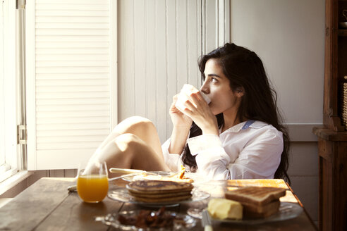 Nachdenkliche Frau trinkt Kaffee am Frühstückstisch zu Hause - CAVF10189