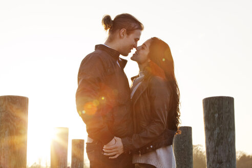 Romantisches Paar bei Sonnenuntergang auf dem Pier stehend - CAVF10213
