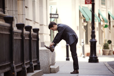 Seitenansicht eines Geschäftsmannes beim Binden von Schnürsenkeln auf einer Straße in der Stadt - CAVF10224