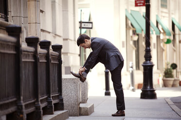 Side view of businessman tying shoelace on city street - CAVF10224