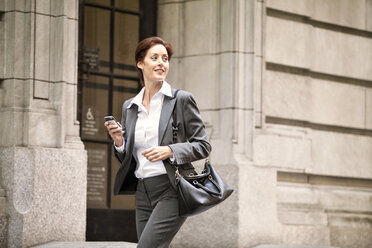 Happy businesswoman looking away while walking on city street - CAVF10233