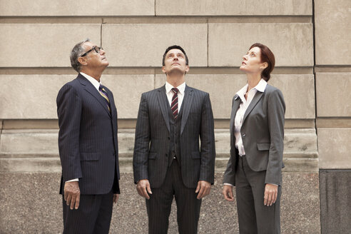 Business people looking up while standing against wall - CAVF10239