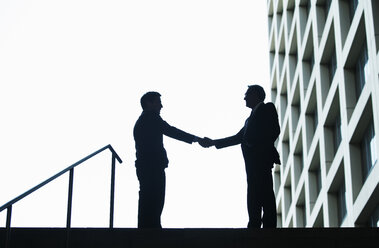 Silhouette of businessmen shaking hands against sky - CAVF10243