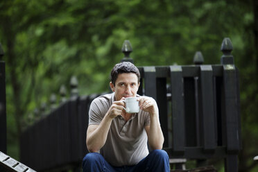 Mann mit Kaffeetasse am Zaun sitzend - CAVF10275