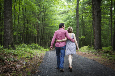 Rückansicht eines Paares, das sich umarmt und auf einem Schotterweg im Wald spazieren geht - CAVF10298