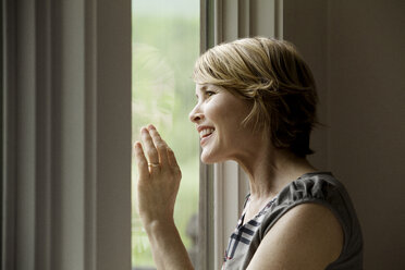 Fröhliche Frau schaut durch das Fenster zu Hause - CAVF10310