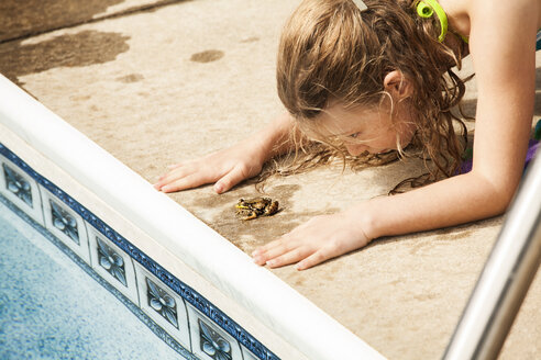 Girl playing with frog at poolside - CAVF10332