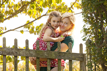 Porträt einer Mutter, die ihre Tochter am Zaun trägt - CAVF10340