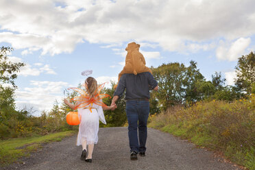 Rückansicht eines Vaters mit Kindern im Halloween-Kostüm, die auf einem Feld laufen - CAVF10346